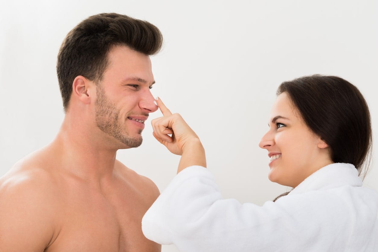 Woman Applying Moisturizer On Man's Nose