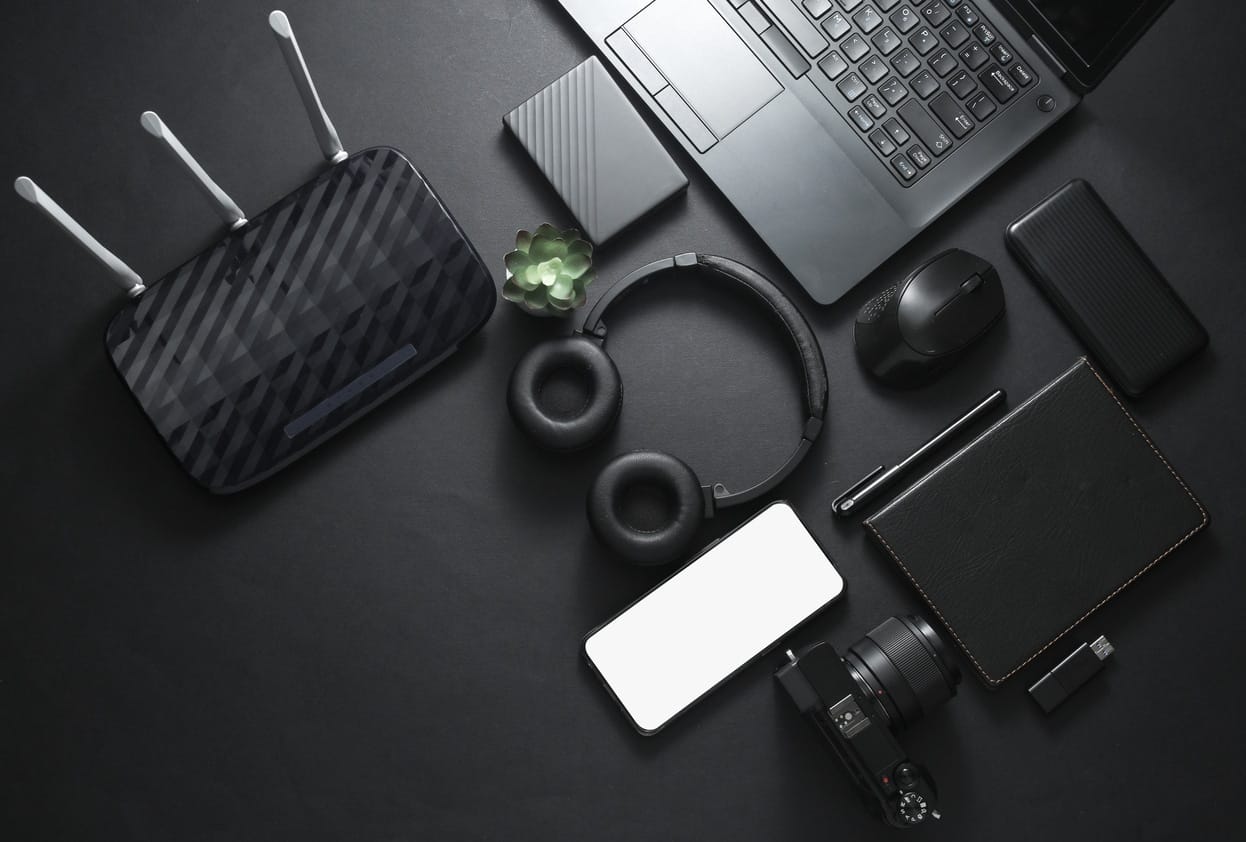 Modern gadgets and accessories in black. Laptop, camera, smartphone, stereo headphones, notepad, external hard drive, USB flash drive on a black background. Photographer Working space. Flat lay. Top view Modern black gadgets and accessories. Laptop, camera, smartphone, stereo headphones, notepad, external hard drive, USB flash drive on a black background.