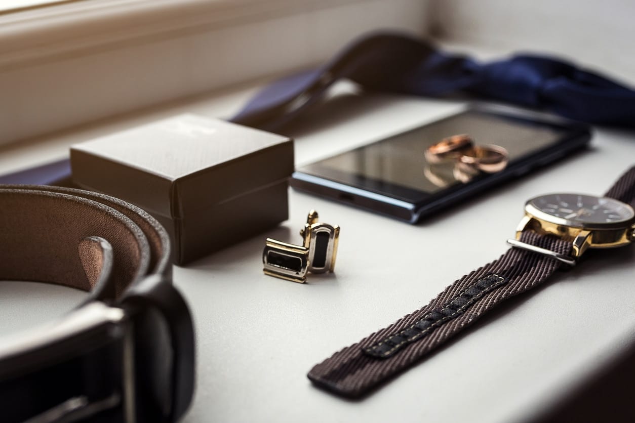 Different men's accessories such as: cufflinks, watches, rings, belt, tie and phone on the table